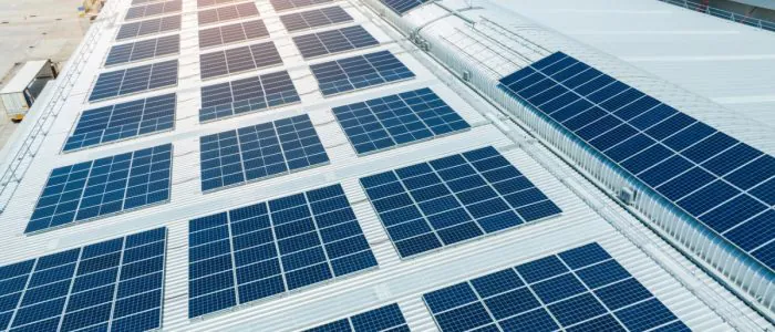 An aerial view of the roof of a large white building covered in multiple rows of solar panels on a sunny day.
