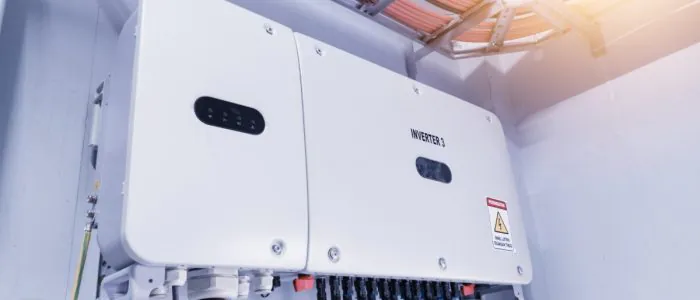 A white box with multiple cables plugged into the bottom, placed high on a wall under multiple orange cables.