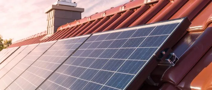 Solar panels with multiple cells placed on a roof with metal brown shingles next to a chimney on a sunny day.