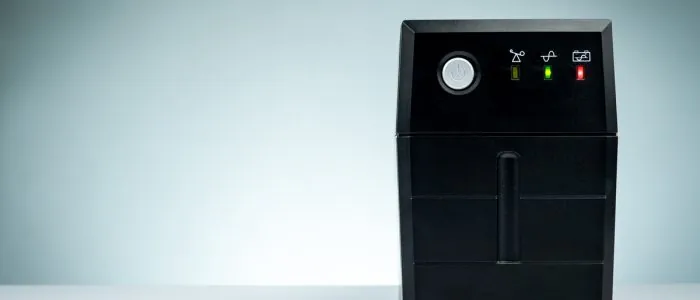 A black powerwall box with a power button and three activity lights placed on a white surface with a white background.