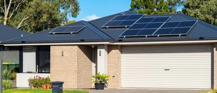 One-story home with a large white garage door, brick walls, and a sloped roof with multiple solar panel units.