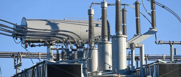 A close-up of the top part of an electrical grid with multiple connectors, cables, and coils, on a sunny day.