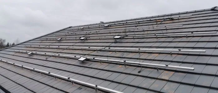 A roof covered in small shingles, with a large metal structure spreading across with small microinverters attached.